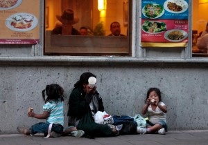 A homeless woman and her children sit outside a restaurant as she waits to receive a handout in Mexico City's historic Zocalo Square